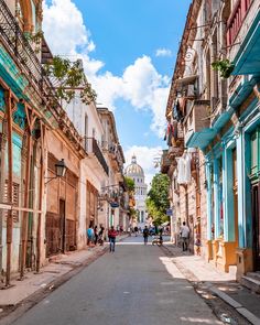 people are walking down the street in an old city with blue and brown buildings on both sides