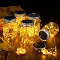 four mason jars with fairy lights in them sitting on a table next to an open book