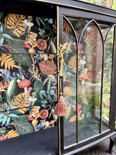 an ornate glass cabinet with floral wallpaper on the front and side panels, decorated with tassels