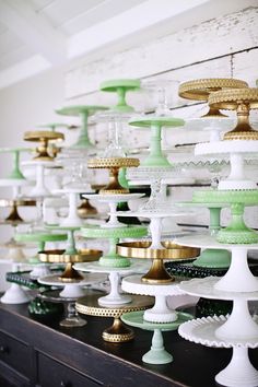 a large collection of green and white glass vases on a black table with gold trim