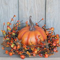 an orange pumpkin sitting on top of a table next to some berries and leaves in front of a wooden fence