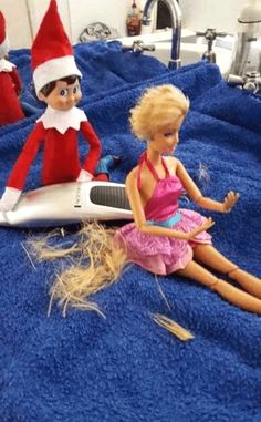 two elf dolls sitting on top of a bed next to an electric hair dryer