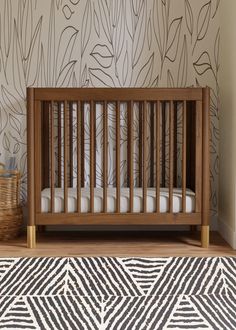 a baby crib in front of a wall with leaves on it and a basket next to it