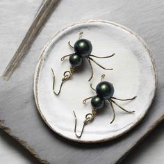 three black pearls are sitting on top of a white plate with gold earwires