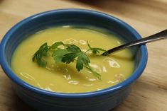 a blue bowl filled with yellow soup and garnished with cilantro leaves