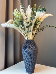 a blue vase filled with white flowers and greenery on top of a table next to a window