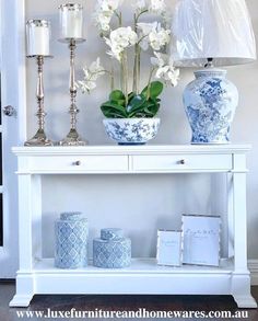 a white table with blue and white vases on it, next to a lamp