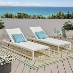 two white lounge chairs sitting on top of a wooden floor next to a blue ocean