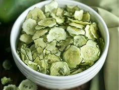 cucumbers in a white bowl on a table next to a green cloth and napkin