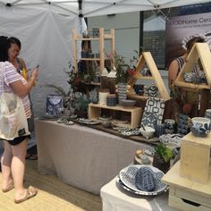 two women standing next to each other near a table with various items on it and people looking at them