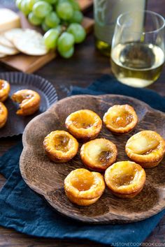 several small pastries on a wooden plate next to some wine glasses and grapes in the background