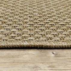 a close up view of a woven rug on a wooden floor with wood planks in the background