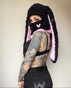 a woman with tattoos wearing a black and pink bunny mask on top of her head