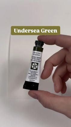 a hand holding a small tube of green ink