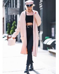 a woman walking down the street wearing black pants and a pink coat with a hat