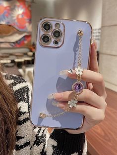 a woman holding up an iphone case with flowers and chains attached to the back of it