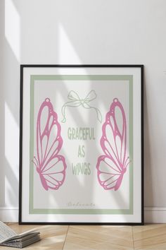 a pink and green butterfly print with the words graceful as wings on it in front of a white wall