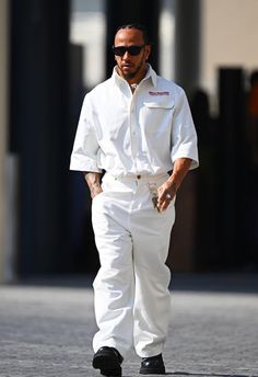 a man in white is walking down the street with his hand on his hip while wearing sunglasses