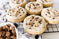 cookies with frosting and chocolate chips on a cooling rack next to a bowl of nuts