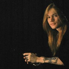 a woman with long hair and tattoos on her arm looking at the camera while sitting in front of a black background