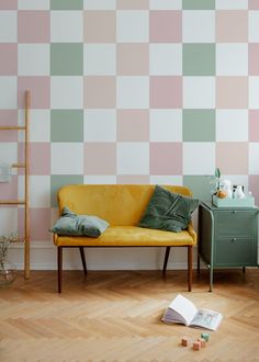 a yellow couch sitting in front of a wall with pink and green squares on it