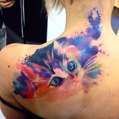 the back of a woman's neck with a colorful cat tattoo on her left shoulder