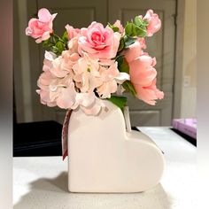 a white vase filled with pink flowers on top of a table