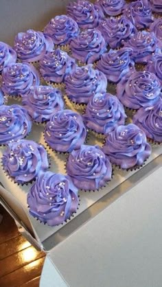 purple cupcakes with frosting in a box on a wooden floor next to a white table