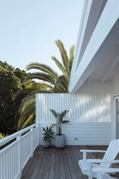 a wooden deck with two white chairs and a potted plant