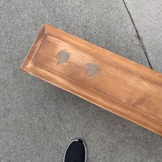 a person standing next to a wooden bench on the sidewalk with their feet propped up