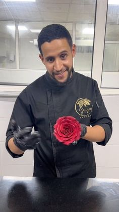 a man in black jacket holding a red rose with gloves on his hands and smiling at the camera