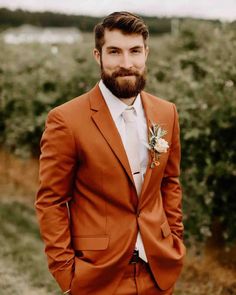 a man with a beard wearing an orange suit and flower in his lapel is looking at the camera