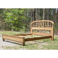 a wooden bed frame sitting on top of a grass covered field in front of trees