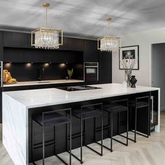 a kitchen with black cabinets and white countertops, an island bar area and chandeliers