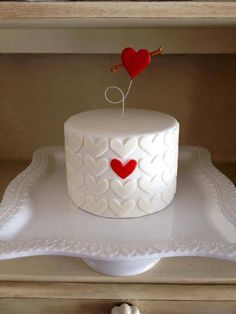 a white cake with a red heart on top and two small hearts in the middle