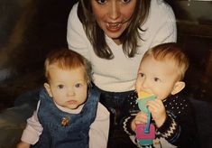 a woman sitting next to two babys and holding a toy in her mouth,