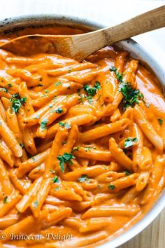 a bowl filled with pasta and sauce on top of a wooden table next to a spoon