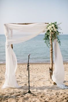 an outdoor wedding setup on the beach with white draping and flowers in vases