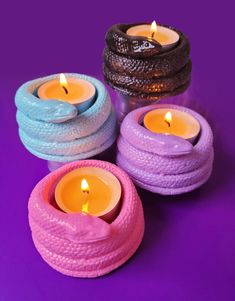 three colorful candles sitting next to each other on a purple surface with one lit candle in the middle