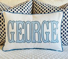 a white and blue pillow with the word george on it sitting on top of a bed