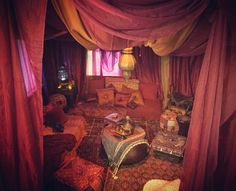 a living room filled with lots of furniture covered in red drapes and hanging lights