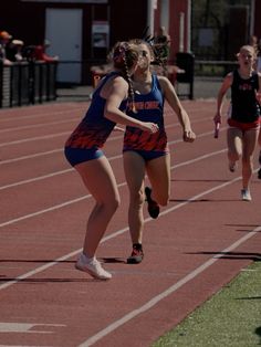 two girls running on a track in the middle of a race, one is wearing blue and red