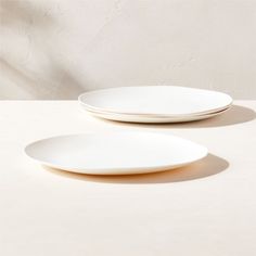 two white plates sitting next to each other on top of a table with one empty plate in the middle