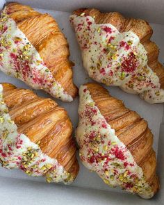 four croissants with white frosting and sprinkles in a box