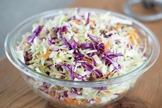 a glass bowl filled with coleslaw on top of a wooden table