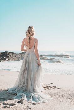 a woman standing on top of a sandy beach next to the ocean wearing a dress