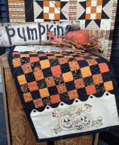 a pumpkin quilt on top of a wooden bench with an old fashioned sign behind it