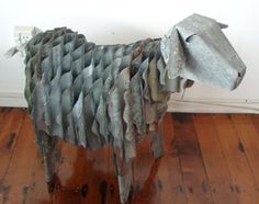 a sculpture of a sheep made out of metal strips on a wooden floor next to a white wall