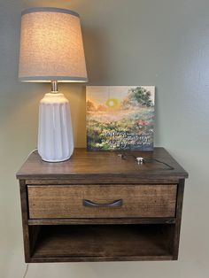 a white vase sitting on top of a wooden table next to a lamp and painting