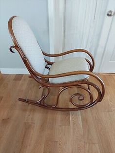 a wooden rocking chair with white cushion on the back and seat, in front of a door